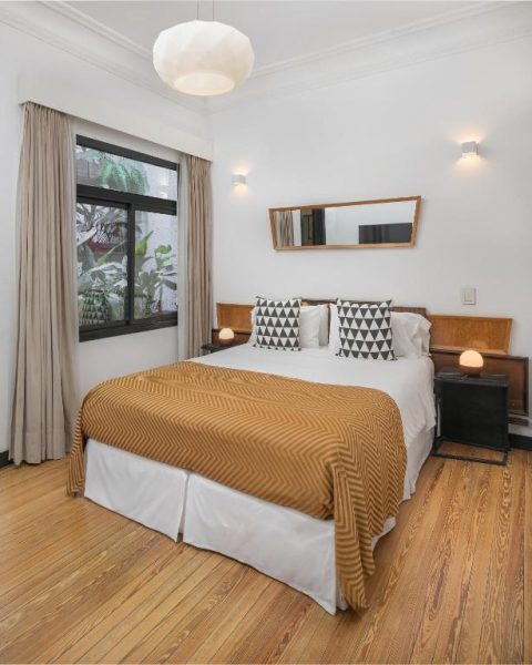 Habitación doble con suelo de parquet y colcha mostaza en FAUNA Montevideo