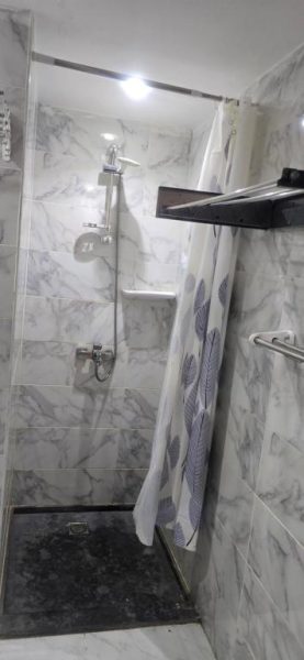 Ducha moderna con revestimiento de mármol blanco y cortina decorativa en Hotel Mirage Bay