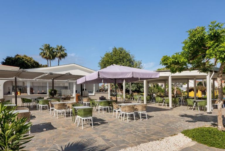 Terraza exterior con mesas y sillas del restaurante del Mayfair Hotel rodeada de palmeras y vegetación