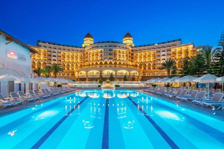 Piscina exterior iluminada del Sidemarin Kirman Premium con tumbonas y fachada del hotel de noche
