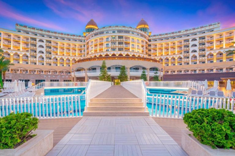 Piscina exterior con pasarela iluminada y lujosa fachada del Sidemarin Kirman Premium en Side, Turquía