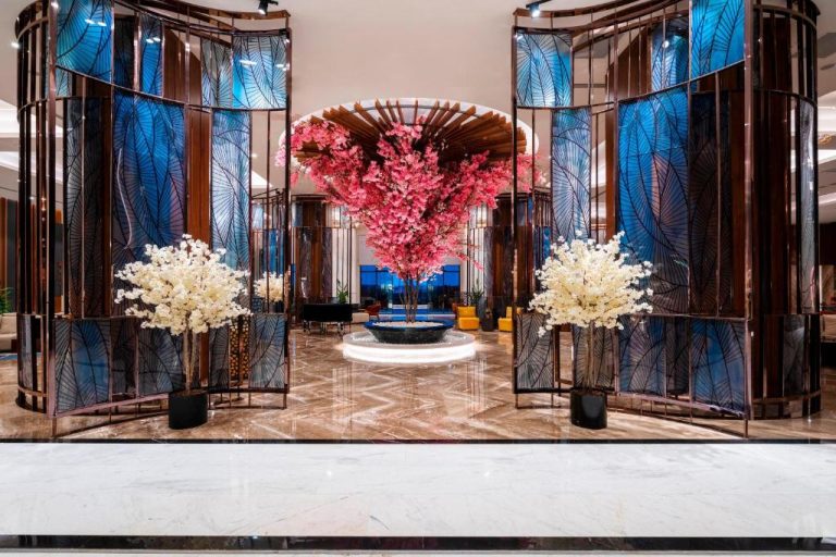 Lujoso lobby del Calyptus Kirman Premium con árbol de flores rosas y columnas decorativas azules
