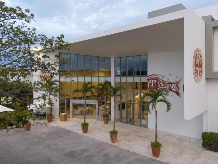 Fachada principal y lobby del Royal Beach Hotel Punta Cana A JdV by Hyatt con palmeras y arte mural