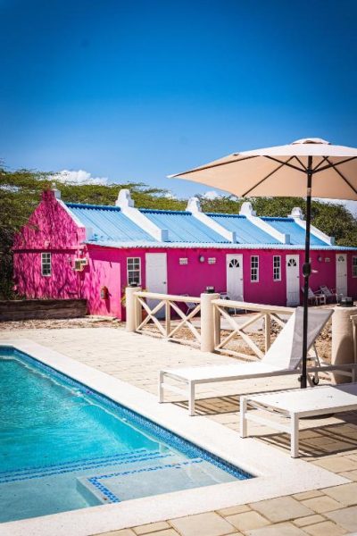 Piscina exterior con tumbonas y sombrilla junto a la colorida fachada rosa del Landhuis Daniel Plantation House
