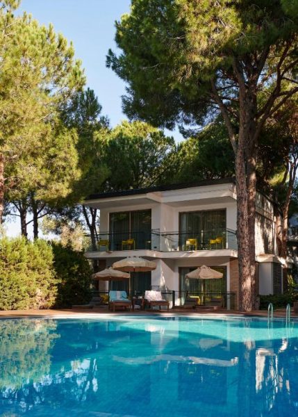 Piscina exterior rodeada de pinos y tumbonas del Voyage Belek Golf & Spa Hotel en Turquía