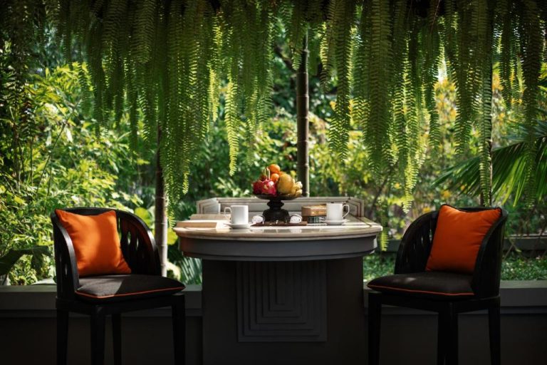 Terraza privada con mesa redonda y sillas con cojines naranja rodeada de jardín tropical en Shinta Mani Angkor