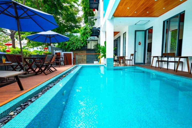 Piscina exterior azul turquesa con terraza de madera y sombrillas en Hoi An Majestic Villa