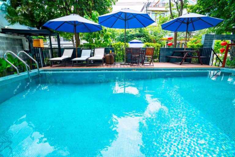 Piscina exterior con tumbonas y sombrillas azules del Hoi An Majestic Villa rodeada de jardín