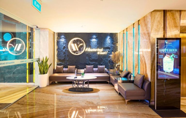 Elegante lobby con sofás de cuero y pantalla Happy Hour en Winsuites Saigon Hotel