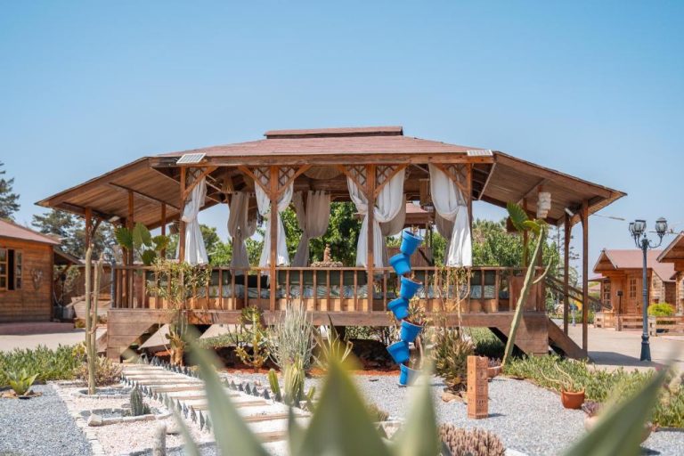 Gazebo de madera con cortinas blancas y jardín de cactus en Lakala Complexe Touristique