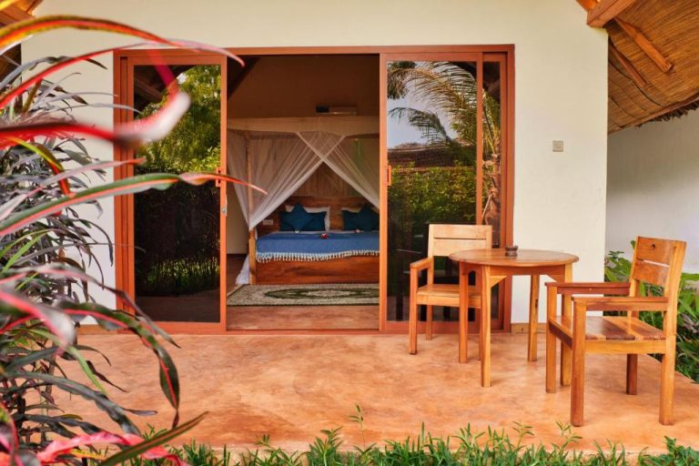 Bungalow con terraza y cama con dosel en Kidoti Bay rodeado de jardín tropical