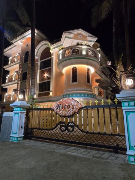 Fachada exterior iluminada del Hotel Nico's con arquitectura clásica y portón de entrada en la noche