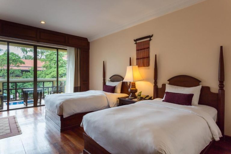 Habitación twin con camas individuales de madera y balcón con vistas al jardín en Prince Angkor Hotel & Spa