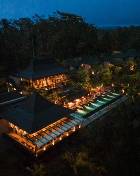 Vista aérea nocturna de la piscina infinita y villas del Ayatara Resort Ubud entre la selva de Bali