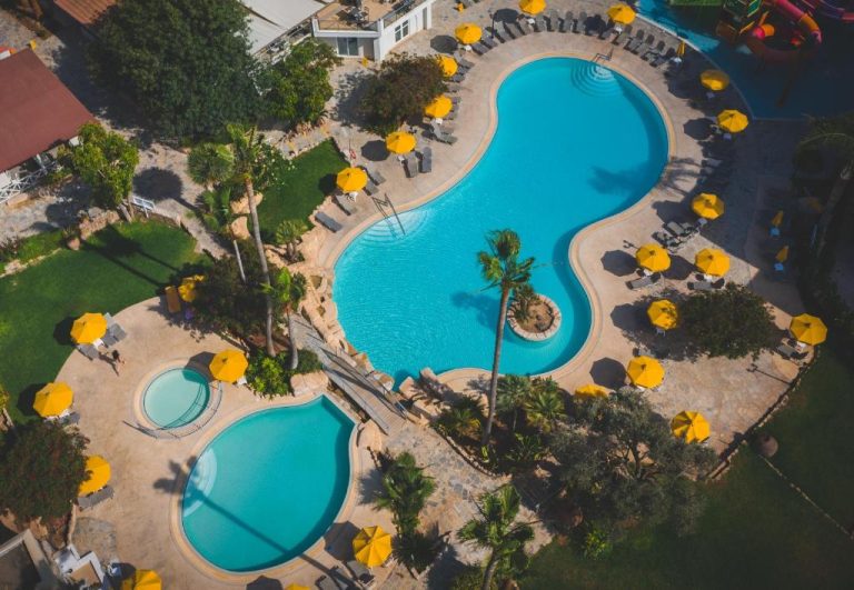 Vista aérea de las piscinas exteriores con sombrillas amarillas y palmeras del Mayfair Gardens