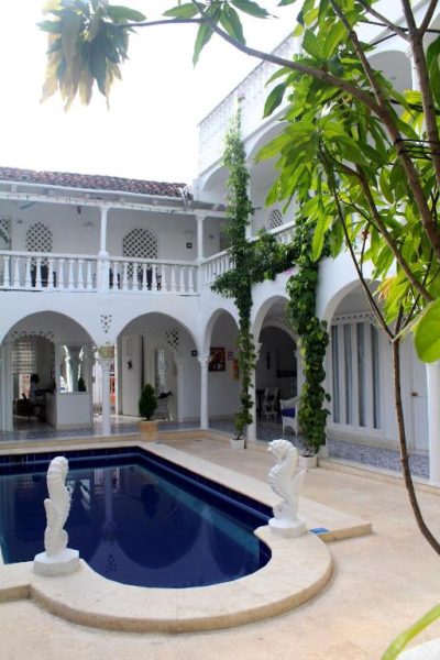 Piscina interior en patio colonial del Hotel Casa Mara by Akel Hotels con arcos blancos y esculturas decorativas