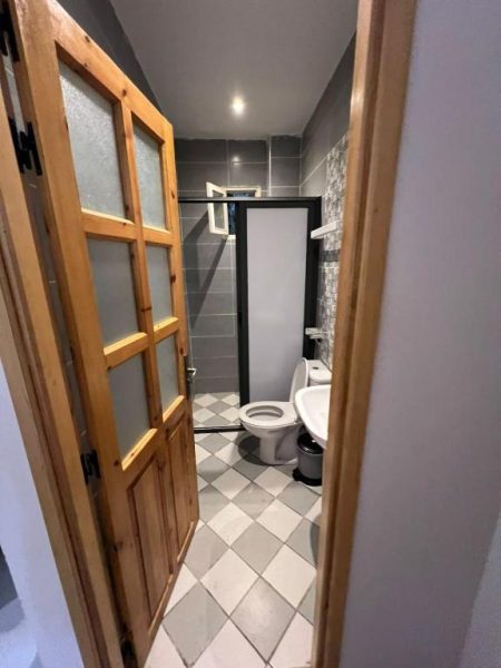 Baño completo con ducha, inodoro y lavabo del BananaHouse con suelo de baldosas en damero