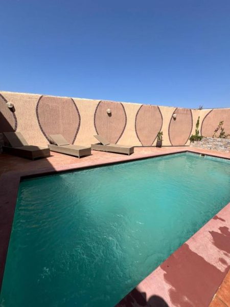 Piscina exterior con tumbonas y muro decorativo del BananaHouse bajo cielo azul