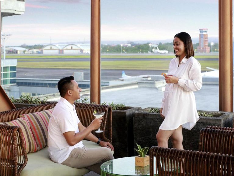 Pareja disfrutando de cócteles en la terraza bar del Novotel Bali Ngurah Rai Airport con vistas a la pista