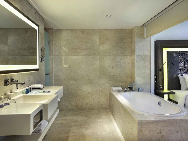 Baño de lujo con bañera empotrada y doble lavabo en mármol del Novotel Bali Ngurah Rai Airport
