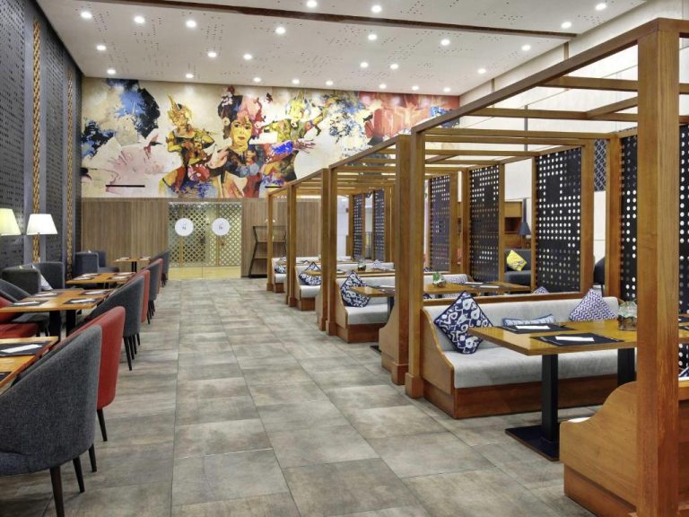 Restaurante interior del Novotel Bali Ngurah Rai Airport con cabinas de madera y mural artístico balinés