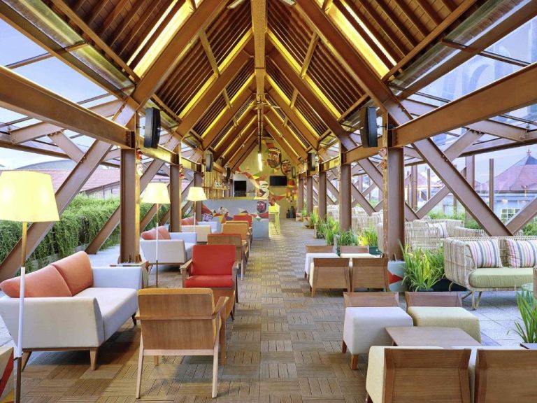 Lobby bar tropical con techumbre de madera y ambiente colorido en Novotel Bali Ngurah Rai Airport
