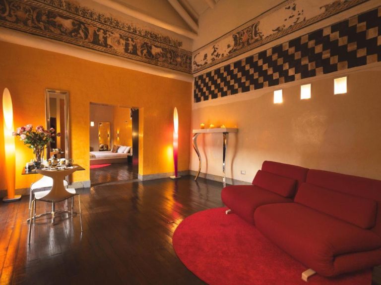 Lujoso salón de suite con sofá rojo y frescos históricos en Casa Cartagena Boutique Hotel & Spa