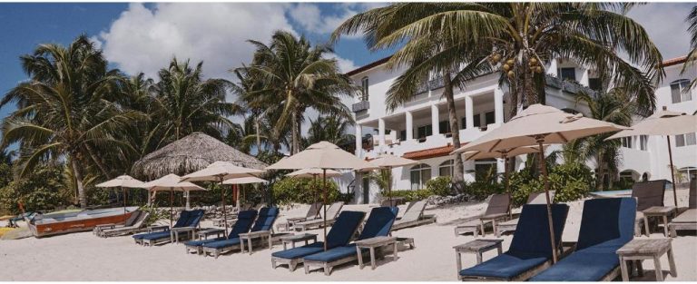 Playa privada con tumbonas azules y sombrillas del Hotel Casa Altamar rodeado de palmeras