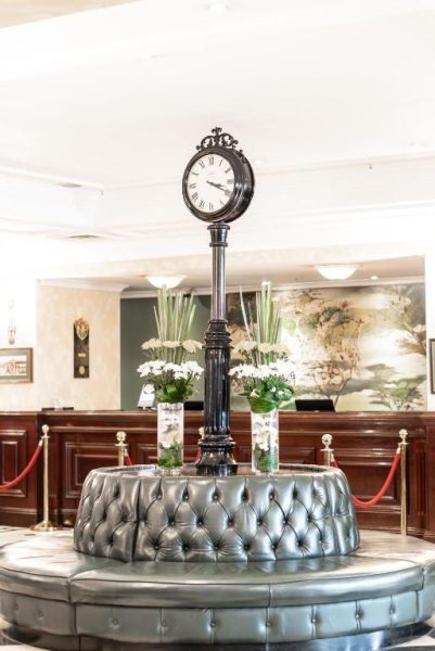 Elegante lobby del Sarova Stanley Hotel en Nairobi con reloj clásico y sofá capitoné plateado