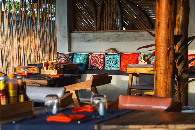 Restaurante terraza con cojines coloridos y mesas de madera en Dhow Beach Boutique Hotel