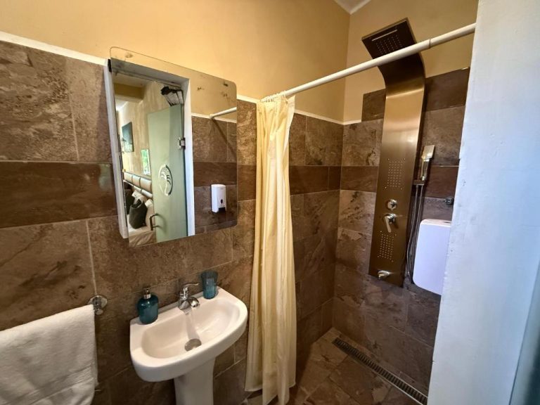 Baño con ducha de lluvia y revestimiento de mármol marrón en Sosua Inn Hotel
