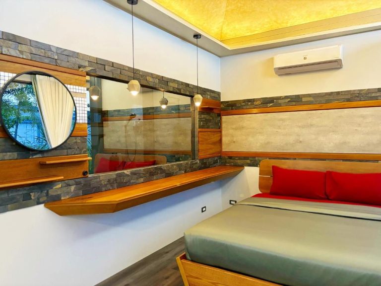 Habitación doble moderna con cama, almohadas rojas y diseño en piedra del hotel Café Luv22