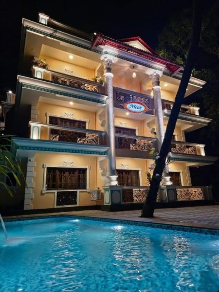 Piscina exterior iluminada de noche en el Hotel Nico's con elegante fachada colonial de tres plantas
