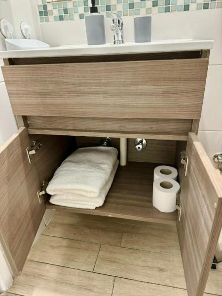 Mueble de baño abierto con toallas blancas y papel higiénico en apartamento Santiago centro