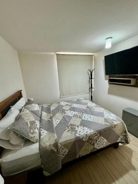 Habitación con cama doble, colcha de patchwork y televisor en apartamento céntrico de Santiago