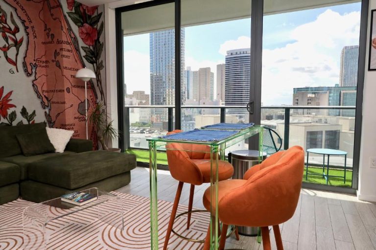 Salón moderno con mesa de cristal y sillas naranjas con vistas al skyline en Downtown Luxe Studio