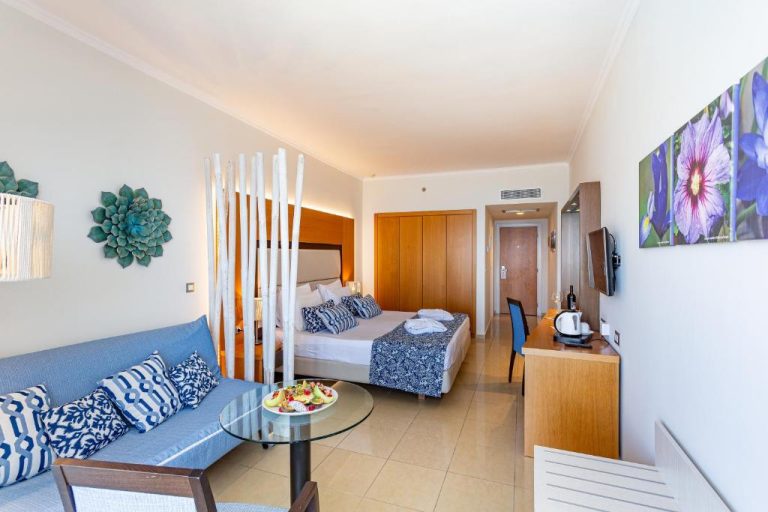 Habitación superior con zona de salón y cama doble decorada en azul del Lindos Bay Hotel
