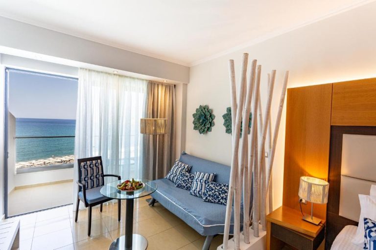 Habitación con sofá azul, zona de estar y terraza con vistas al mar en Lindos Bay Hotel