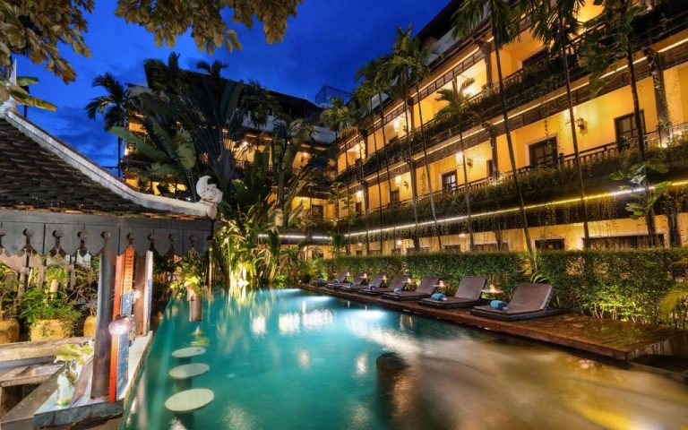 Piscina exterior iluminada de noche con tumbonas en el Residence Indochine Suite de Siem Reap