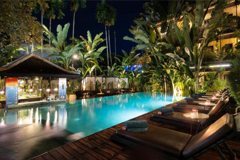 Piscina exterior iluminada de noche con tumbonas y bar tropical en Residence Indochine Suite