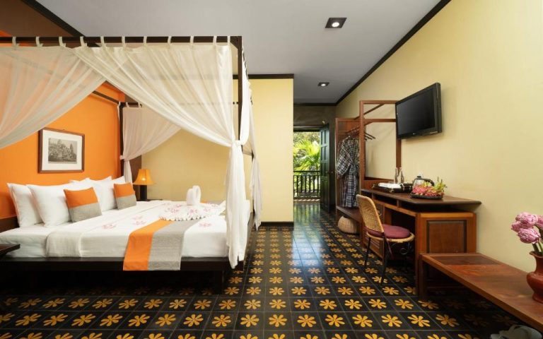 Habitación con cama de dosel y decoración colonial del Residence Indochine Suite con balcón y suelo ornamental