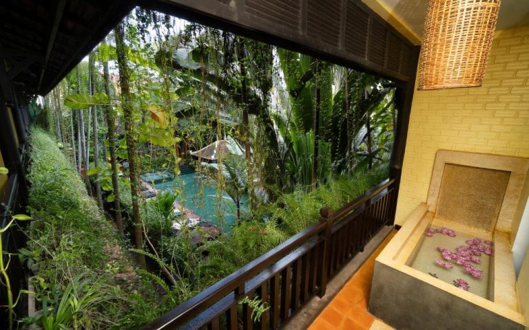 Terraza con bañera de flores y vistas a la piscina rodeada de vegetación tropical en Residence Indochine Suite