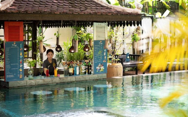 Bar junto a la piscina exterior del Residence Indochine Suite rodeado de vegetación tropical