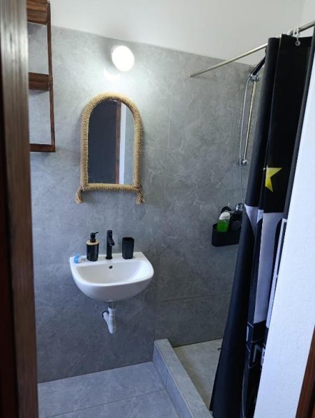 Baño moderno con lavabo, espejo de mimbre y ducha en el B&B Casa Boho