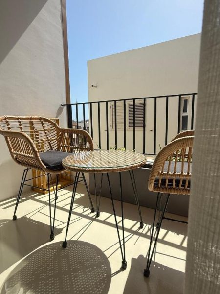 Terraza soleada con sillas y mesa de ratán en OOLAA Trendy Accommodation, ideal para relajarse al aire libre