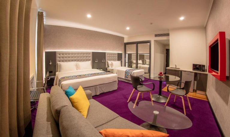 Suite doble moderna con sofá, alfombra morada y TV en el Fairway Colombo, hotel tecnológico en Sri Lanka