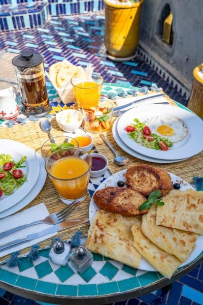 Desayuno marroquí completo con zumo de naranja, huevos y msemen en la terraza del Riad Serendip