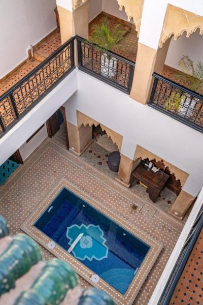 Patio interior con piscina de mosaicos y balcones de forja del Riad Serendip en Marrakech