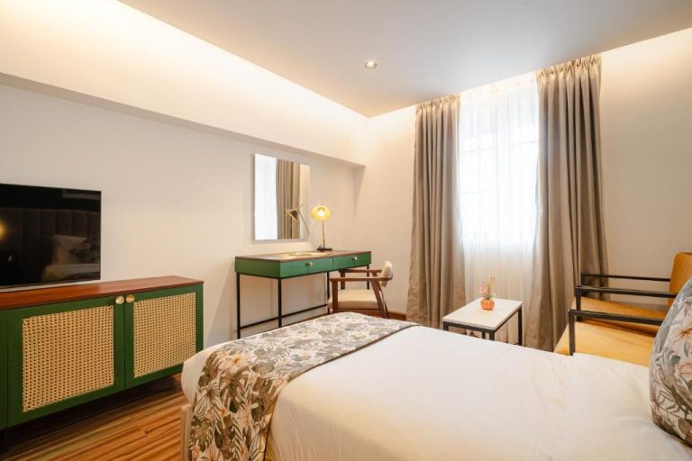 Habitación doble con cama, escritorio verde y televisión del hotel MK Colombo en Sri Lanka