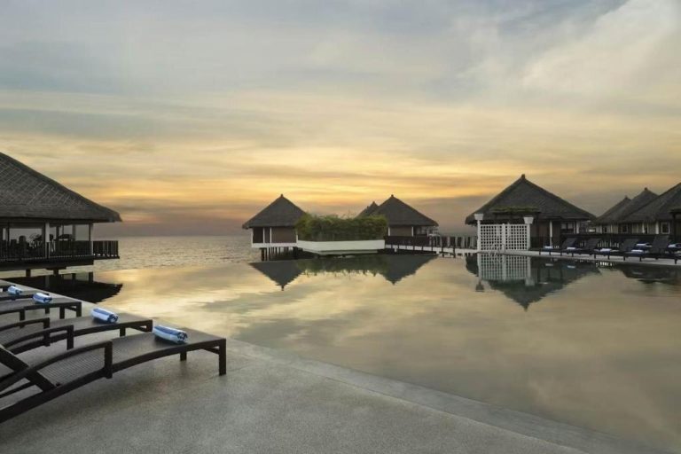 Piscina infinita con bungalows sobre el agua al atardecer en Golden Palm Tree Suite Sepang Malasia
